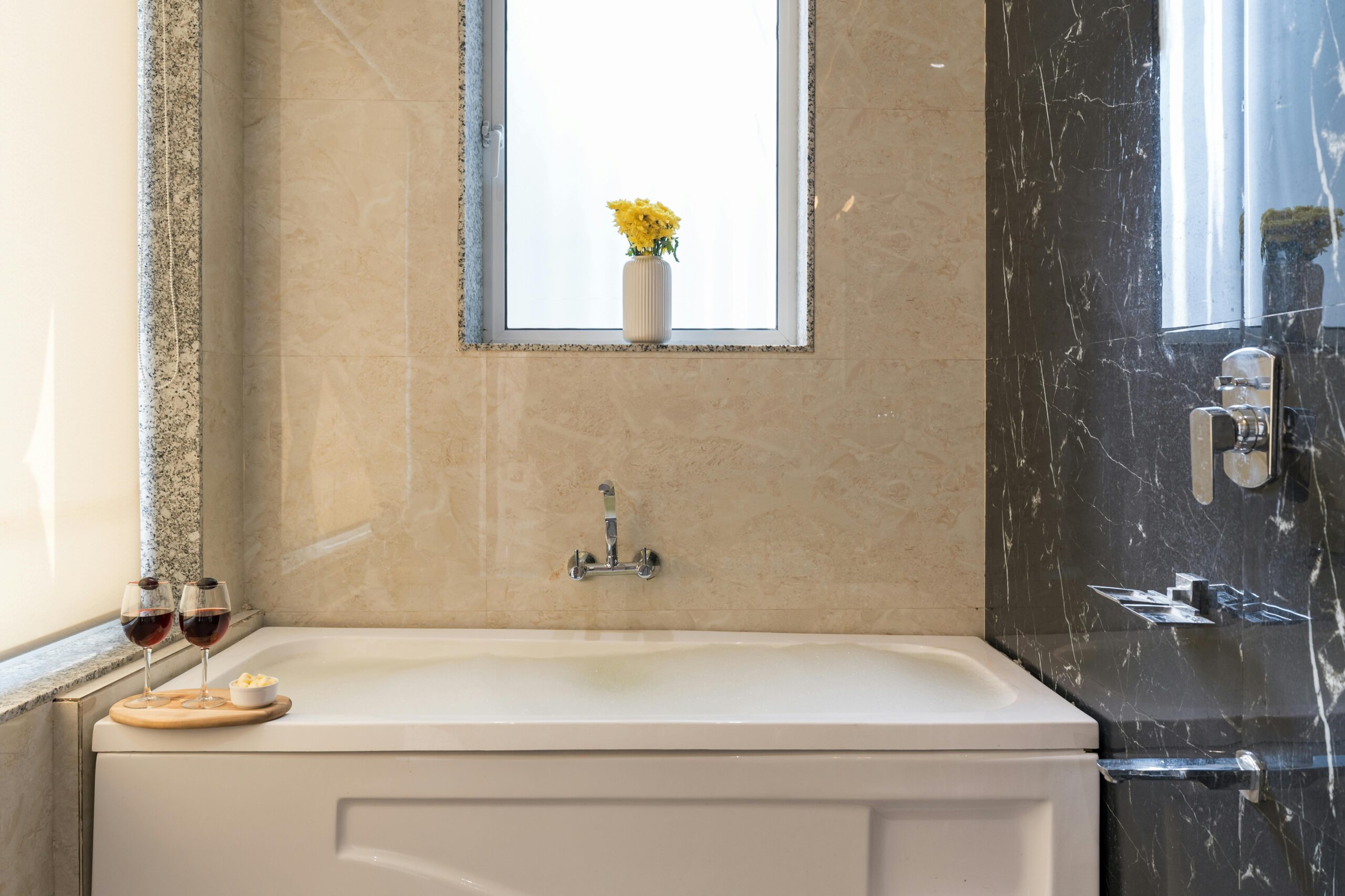 About - Beautiful, Stunning Bathroom Transformations by Expert Renovator Elegant bathroom with marble walls, bathtub, flowers, and wine glasses.