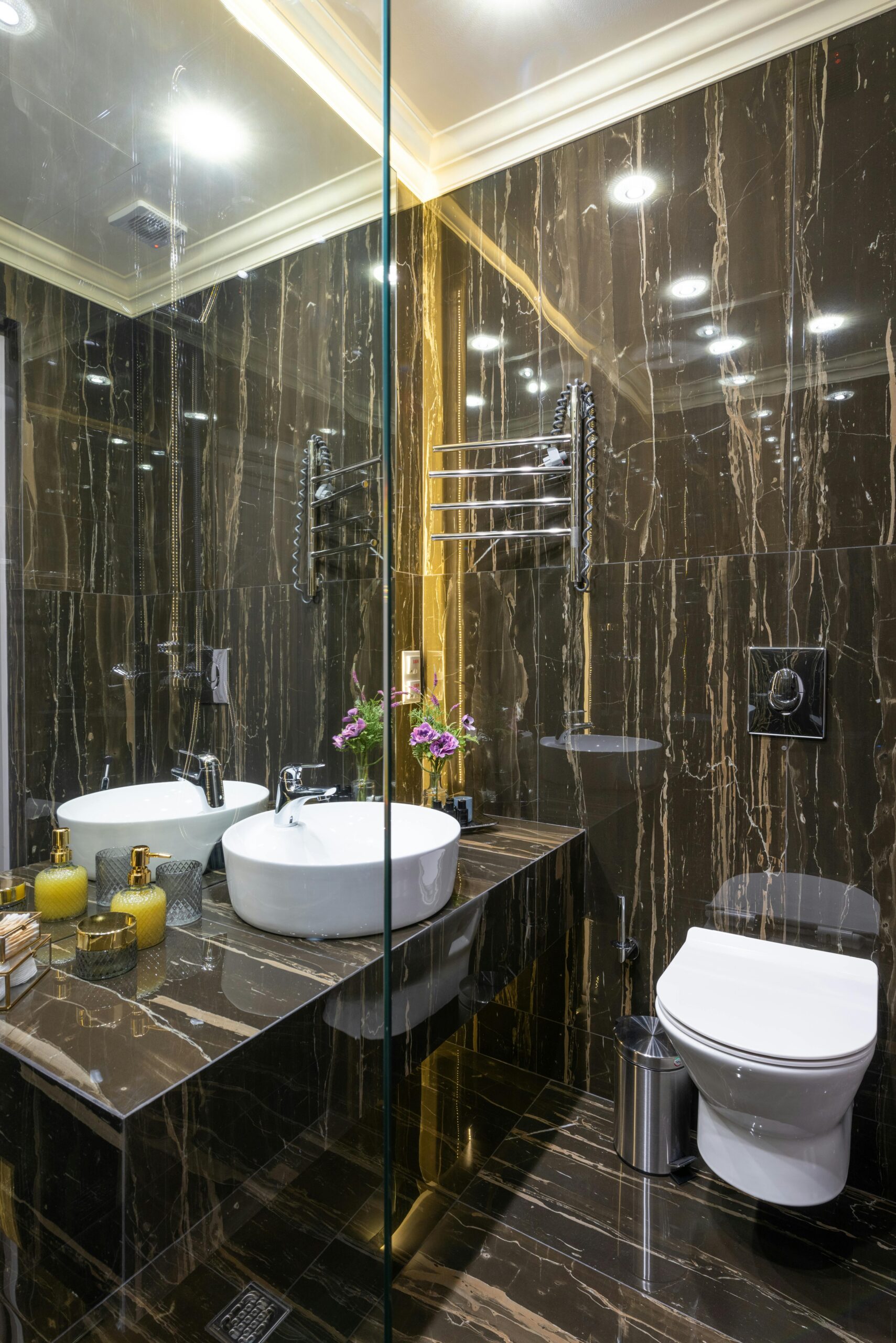 About - Beautiful, Stunning Bathroom Transformations by Expert Renovator Modern bathroom with toilet bowl against washbasin and toiletry products reflecting in mirror under luminous lamps